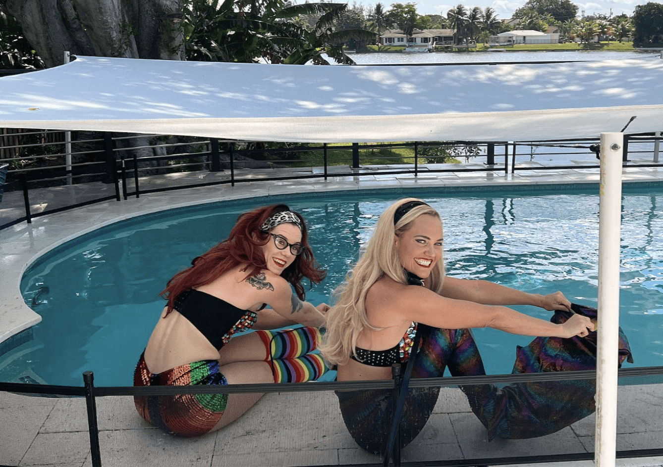 Two female swimmers, one blond, one redhead, in mermaid costumes in front of a pool.
